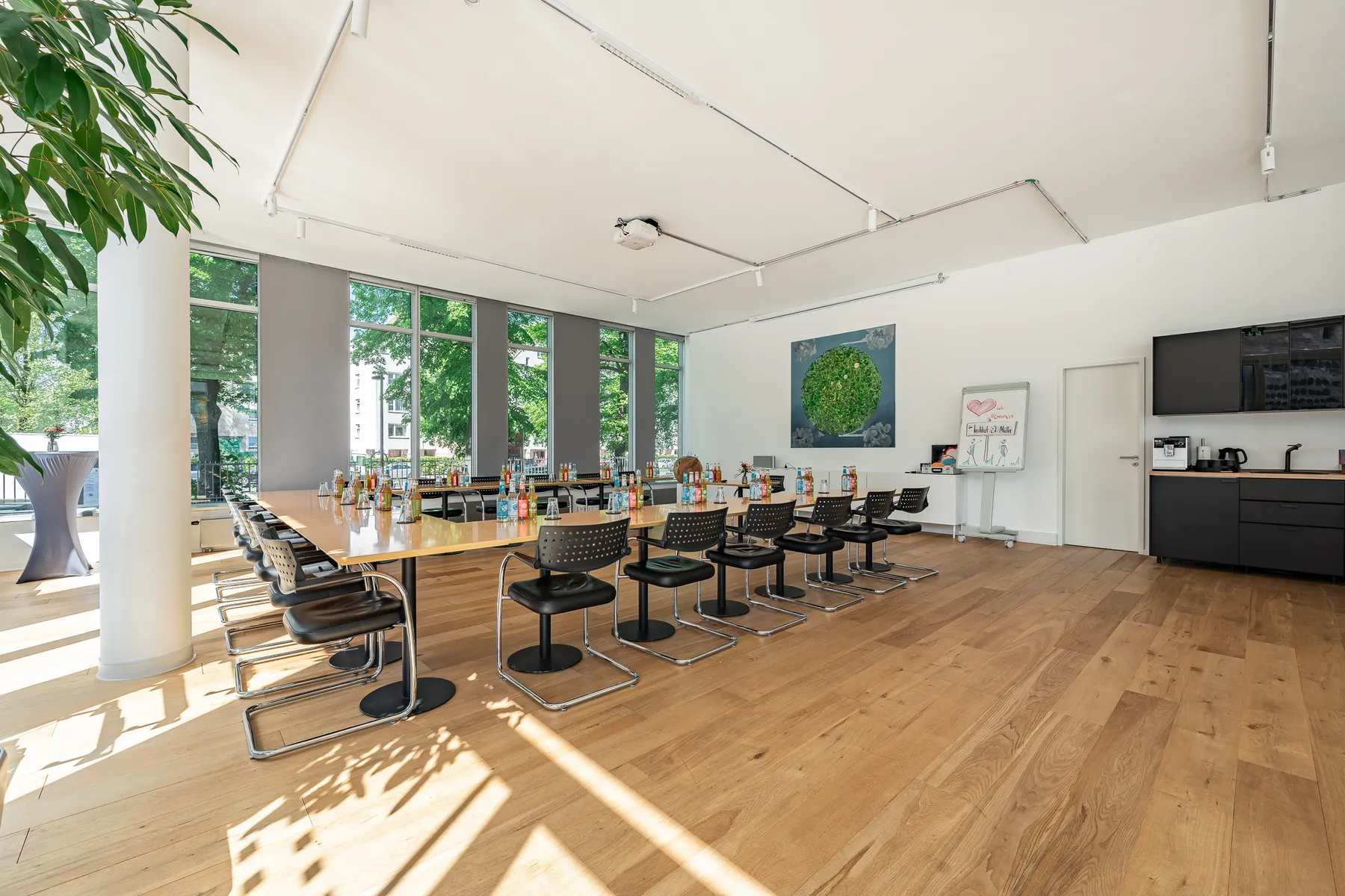Heller Seminarraum des Instituts mit langer Tischreihe, Freischwingern, Flipchart und bodentiefen Fenstern zu einer baumbestandenen Straße.