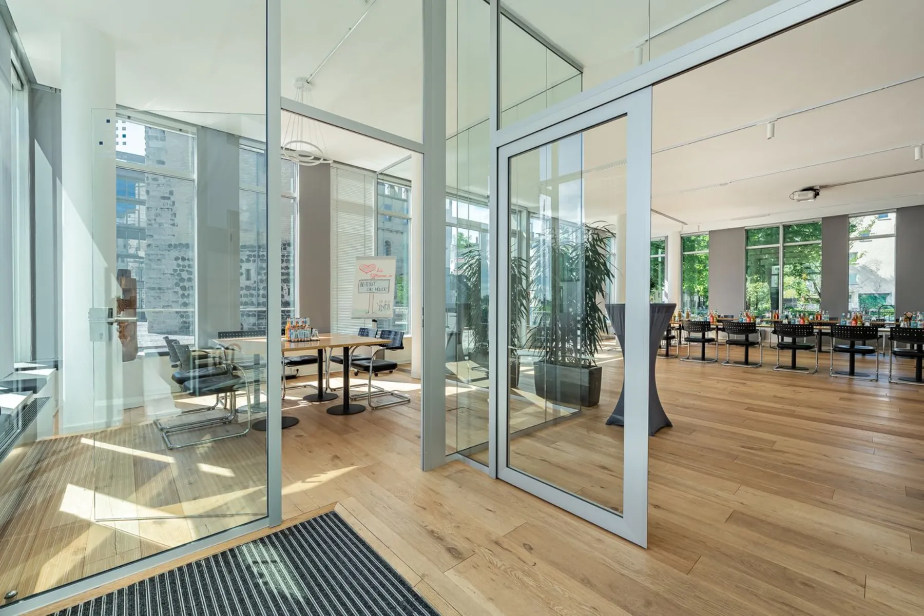 Foyer des Instituts mit Eichenparkett und Glaswänden, links der kleine Besprechungsraum, rechts der offene Seminarbereich mit Stehtisch und Stuhlreihen.